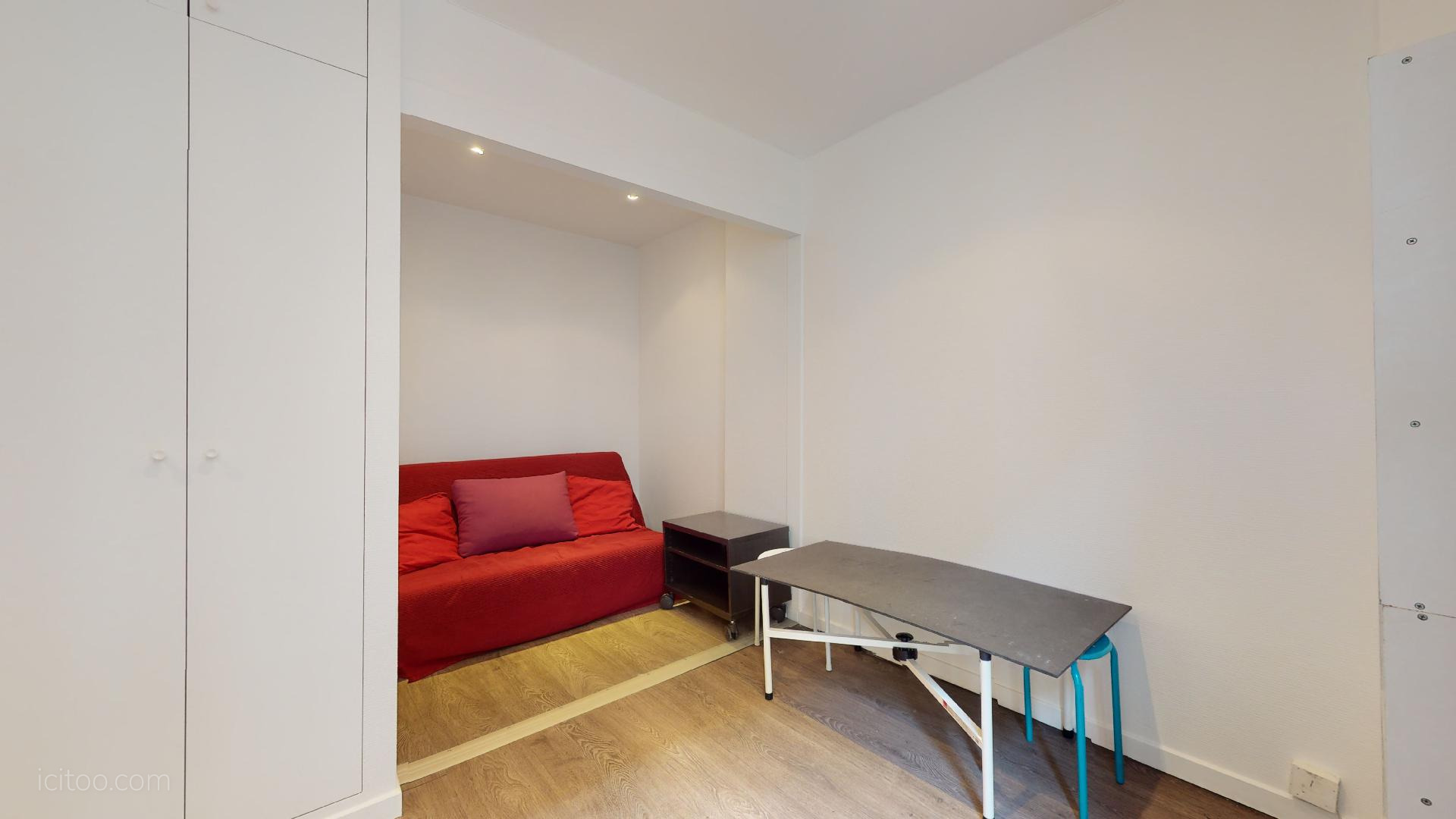 Studio à louer Paris 75001 : espace de vie avec canapé convertible et table pliante, vue sur le coin nuit.