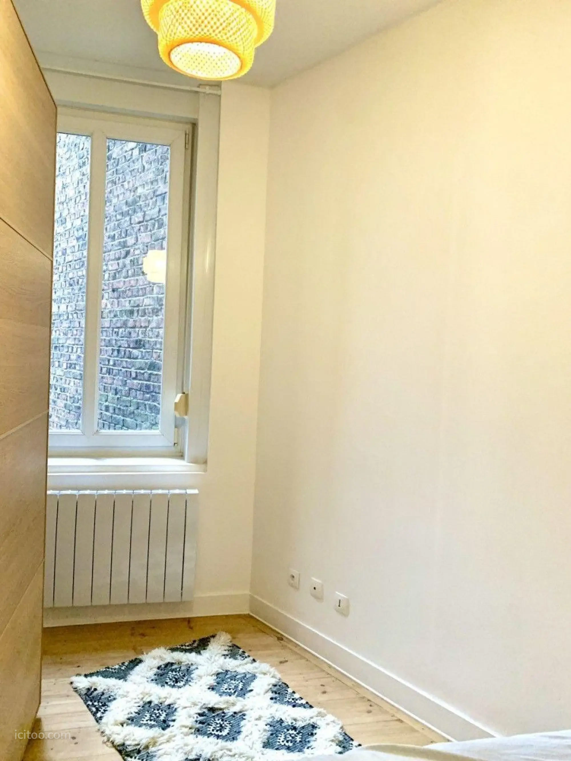 Chambre d'appartement T2 avec fenêtre, radiateur neuf et tapis décoratif, à louer à Lille.