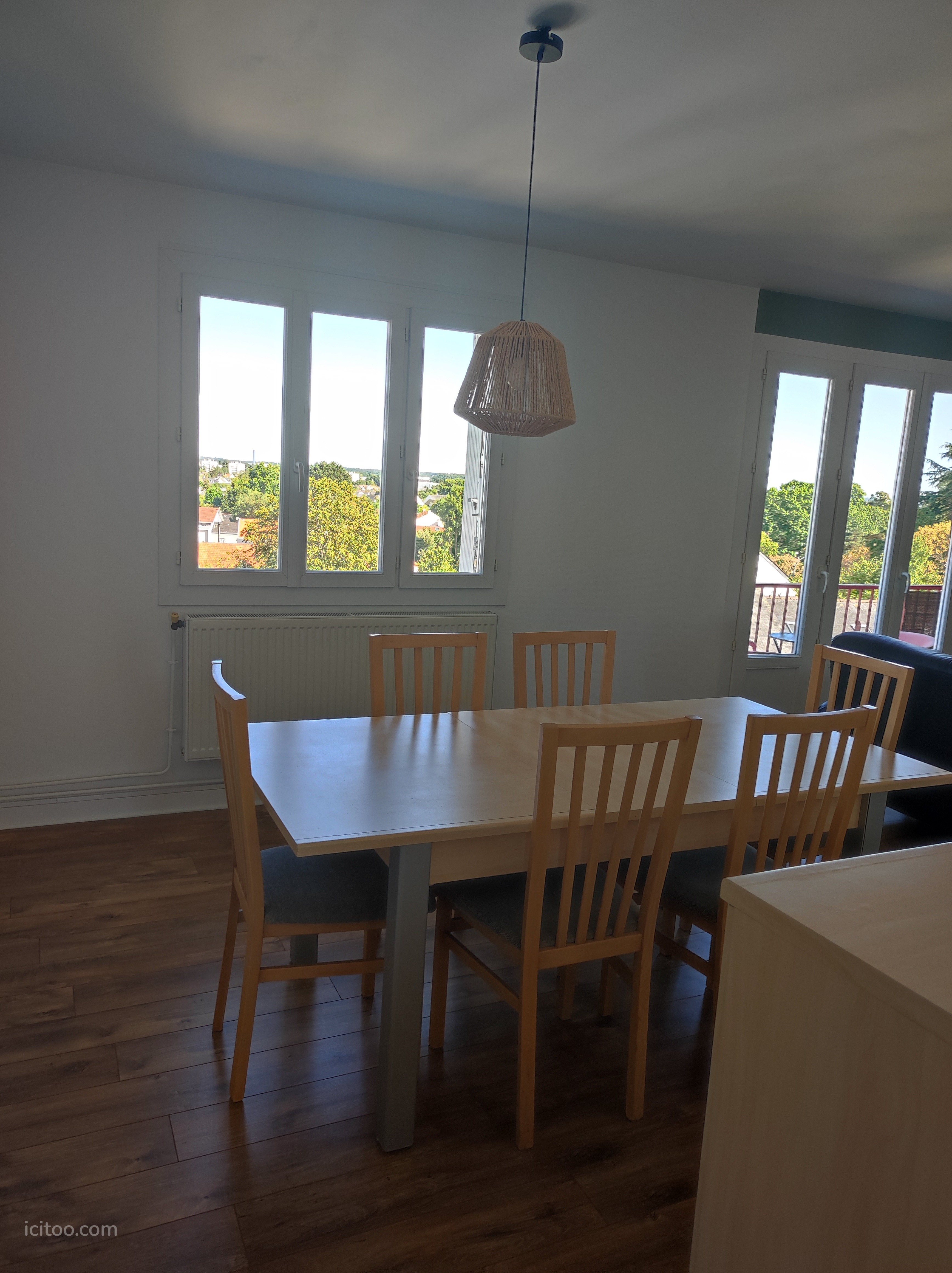 Salle à manger avec table en bois et chaises, vue sur l'extérieur par les fenêtres, appartement à louer à Nantes.