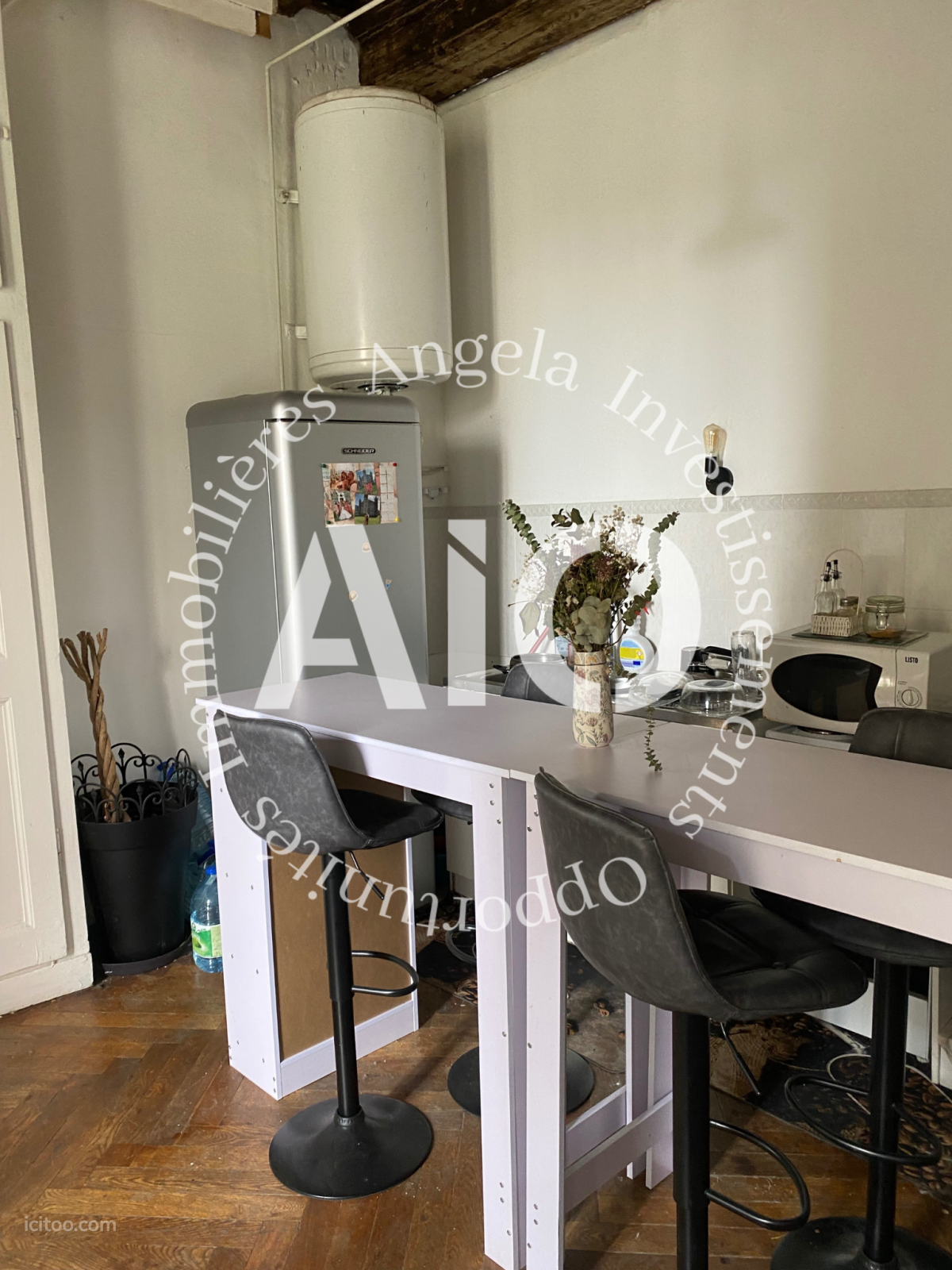 Cuisine aménagée avec réfrigérateur, table haute et tabourets dans un studio à Lyon.